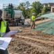 Hydromulch crew sprays fiber mulch over a construction slope while contractors review the erosion control plan and installation scope