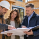 Project owner, contractor and lender reviewing construction progress and draw documents beside a partly completed home
