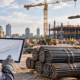 Construction estimator reviews steel price trends beside reinforcing bars and structural beams at an active project site