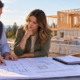 A prospective homebuilder and lender review construction plans and a project budget beside a residential foundation.