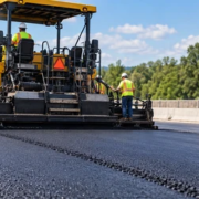 Asphalt paver spreads hot mix asphalt while a road roller compacts the new pavement lane.