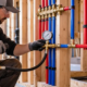 Plumber using a pressure-test pump and gauge to check red and blue PEX water lines before the wall is closed.
