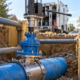 A water-main tapping machine connects to a sleeve and valve on a blue water main in a shored trench.