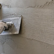 Worker embeds woven scrim reinforcement mesh into wet plaster on a construction wall