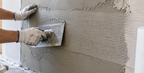 Worker embeds woven scrim reinforcement mesh into wet plaster on a construction wall
