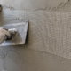 Worker embeds woven scrim reinforcement mesh into wet plaster on a construction wall