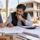 Construction estimator and contractor compare building plans, quantity schedules, cost worksheets, and material samples at a house construction site