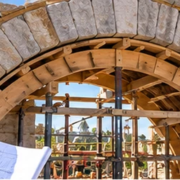 Mason and architect inspect a curved stone arch under temporary support, illustrating arch construction and its structural form.
