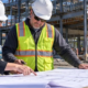 Architect and contractor collaborate over blueprints at an active building site, coordinating design decisions with construction work.