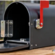 Open architectural mailbox shows its hinge and latch beside replacement screws and hardware on a workbench.