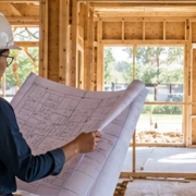 Architect checks a house framing plan while a contractor examines the framed openings, connecting design documents to construction work.
