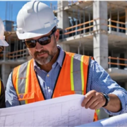 Architect and construction manager compare a blueprint with the building frame under construction behind them, illustrating design and execution working together.