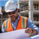 Architect and construction manager compare a blueprint with the building frame under construction behind them, illustrating design and execution working together.