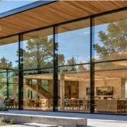 Modern glass-fronted building with its bright interior visible through transparent glazing and trees reflected across the façade.