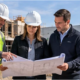 Construction company team reviews project plans with a client at a site where residential and commercial buildings are in progress.