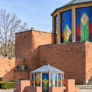 Architect examines a model beside a colorful brick and glass Expressionist pavilion inspired by Bruno Taut.