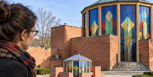 Architect examines a model beside a colorful brick and glass Expressionist pavilion inspired by Bruno Taut.
