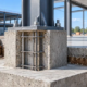 Reinforced concrete pedestal on a footing supporting a steel column base plate with anchor bolts.