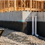 Civil engineer checks site grading and foundation drainage beside a framed house.