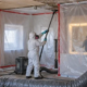 Protected asbestos remediation work in a commercial building behind sealed containment with negative-air equipment and suited abatement workers.