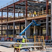 Project manager surveys a complex commercial building site with a steel frame, concrete structure, and coordinated mechanical systems.