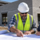 Construction manager and property owner review plans and a cost worksheet beside a commercial building under construction.