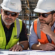 Experienced commercial construction superintendent mentors a project manager while reviewing plans at an active building site.