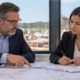 Property developer and lender review commercial construction plans and financing documents beside a project site, with no amounts shown.