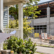 Homeowner and project planner review a neighboring commercial development plan from a porch while construction proceeds behind the property boundary.