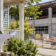 Homeowner and project planner review a neighboring commercial development plan from a porch while construction proceeds behind the property boundary.