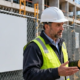Site manager discusses project information with a nearby resident at a commercial construction fence beside a blank notice board.