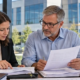 Property owner and accountant review construction invoices and building plans beside a completed commercial office, organizing project-cost records.