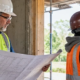 Architect reviews drawings while a contractor checks a wall opening at an active building site, showing their different design and construction roles.