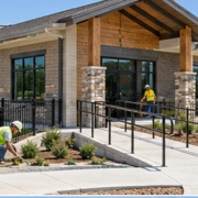 Daycare building under construction with an accessible entrance ramp, fenced play yard, and workers finishing the low-rise facility.