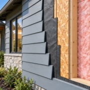 Cutaway of a house exterior wall showing siding, a weather barrier, sheathing, insulated timber framing, and interior finish.