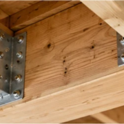 Metal floor joist brackets secure intersecting timber joists to a support beam, with fastening holes visible.