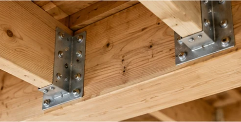 Metal floor joist brackets secure intersecting timber joists to a support beam, with fastening holes visible.