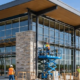 Crew installs storefront glazing and exterior cladding on a broad grocery-store building with a covered entrance canopy.