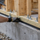 Installer checks anchor bolts and level at the sill plate joining a wood-framed wall to its concrete foundation.