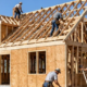 Carpenters assemble standardized timber framing and roof trusses on a postwar suburban Cape Cod house under construction.