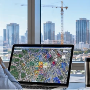 Project manager checks a city map and nearby building projects from an office overlooking active commercial construction.