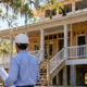 Architect and builder review plans for a raised Louisiana cottage under construction, with a broad porch and elevated foundation.