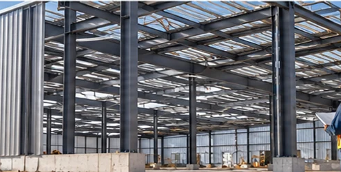Steel frame and metal roof and wall panels form a commercial metal building under construction as a worker checks the structure.