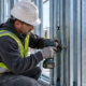 Installer fastening galvanized light-gauge steel studs and track to form a straight wall frame on a construction site.