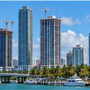 Miami-Dade waterfront skyline with active residential and commercial towers, construction cranes, and palm trees in tropical daylight.