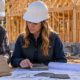 Homebuilder and estimator review material samples and plans beside a framed house in Michigan during autumn.