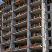 Multi-storey apartment building under construction with concrete floors, open balcony bays, and a tower crane.