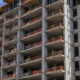 Multi-storey apartment building under construction with concrete floors, open balcony bays, and a tower crane.