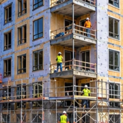 Mid-rise multi-unit apartment building takes shape behind scaffold as crews construct repeated floors and balconies.