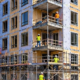 Mid-rise multi-unit apartment building takes shape behind scaffold as crews construct repeated floors and balconies.